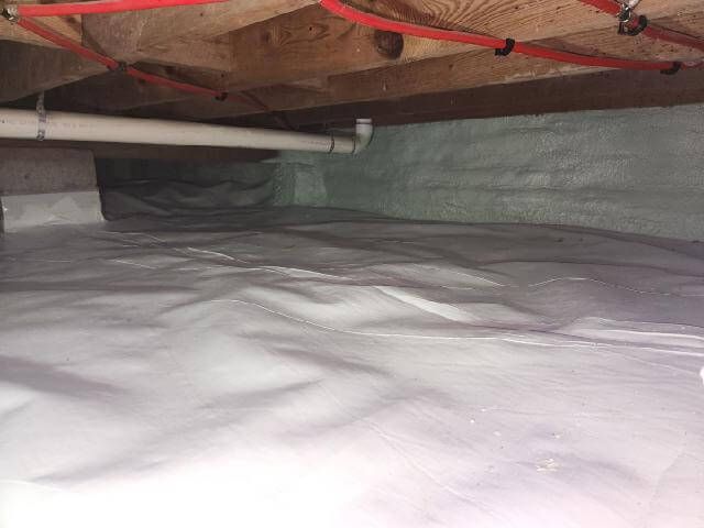A Portland-area crawl space after encapsulation: clean reinforced vapor barrier sealed across the soil and up the foundation walls, perimeter vent visible in the wall